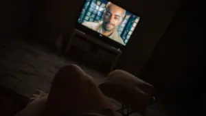 Ciemny pokój z włączonym telewizorem, na którym widać twarz mężczyzny.