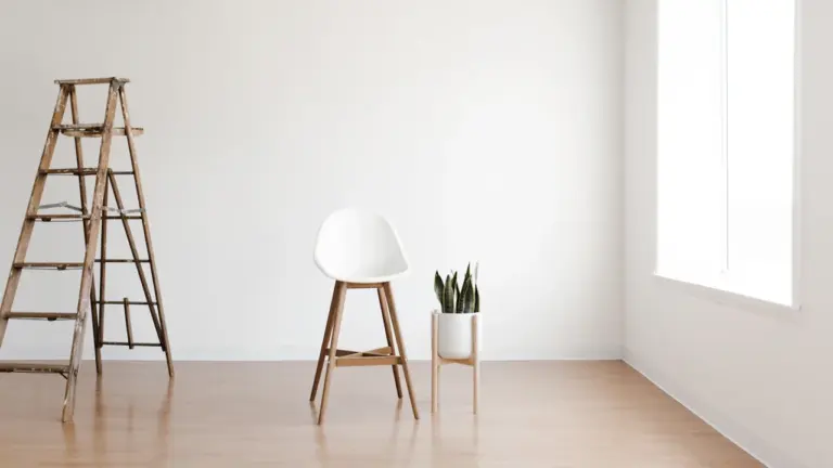 Minimalistyczne, puste pomieszczenie z drewnianą drabiną, krzesłem i zieloną rośliną w doniczce.