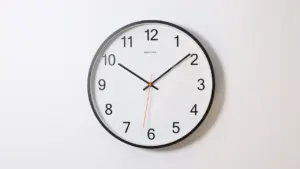 Okrągły zegar ścienny z czarnymi wskazówkami na jasnym, minimalistycznym tle.